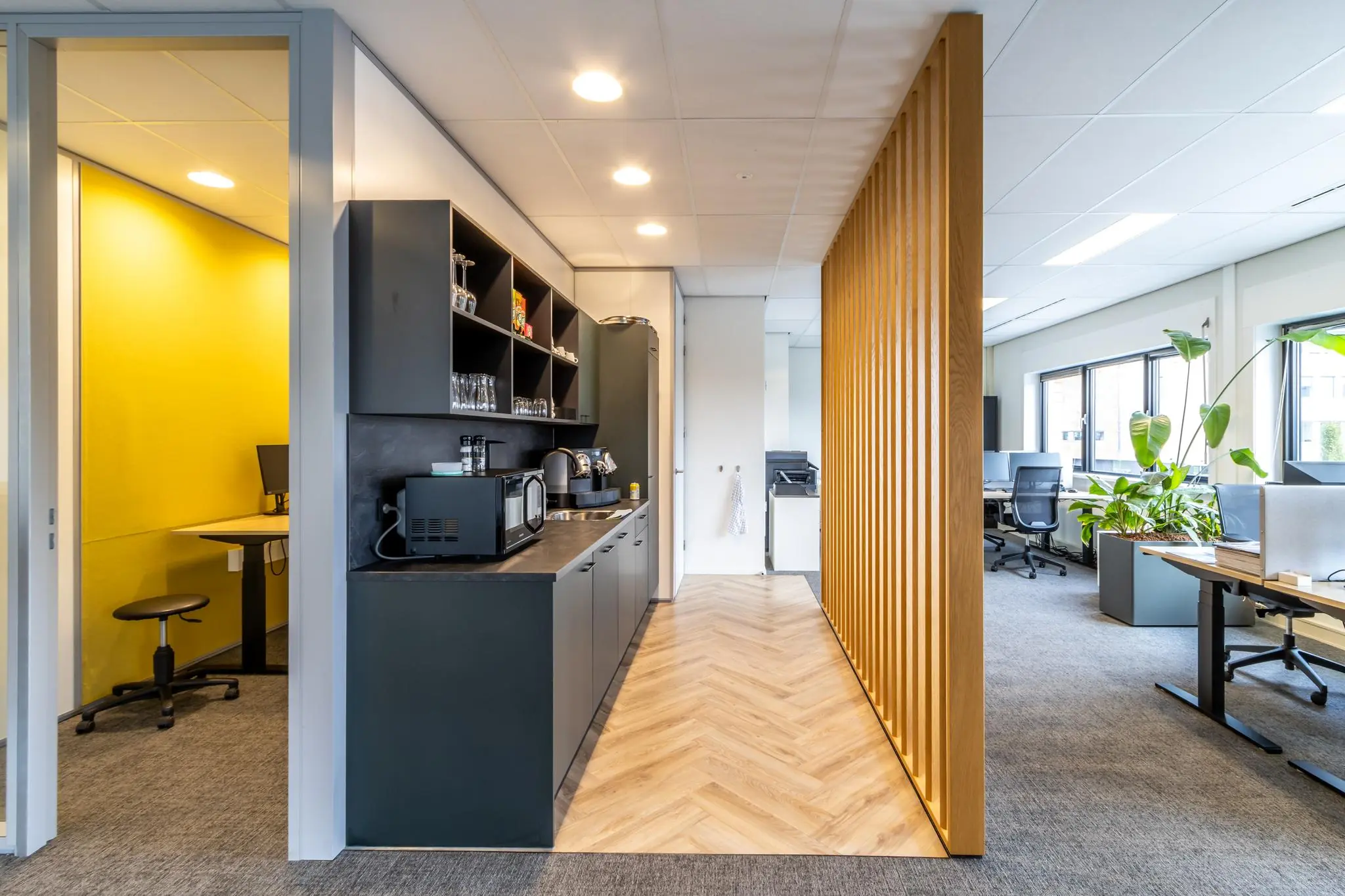 Moderne kantoorruimte aan de Lage Biezenweg met open werkplekken, een kitchenette en een gele vergaderruimte.